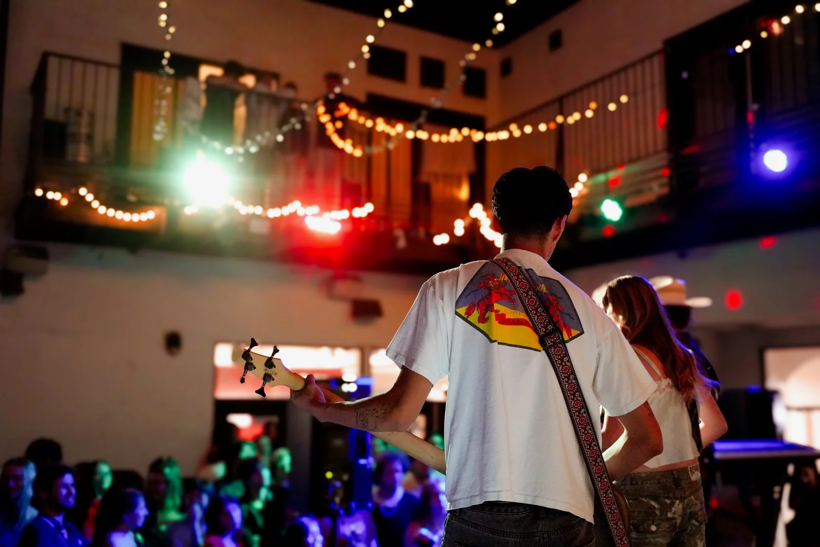 The band seen from behind, facing the audience under amber string lights