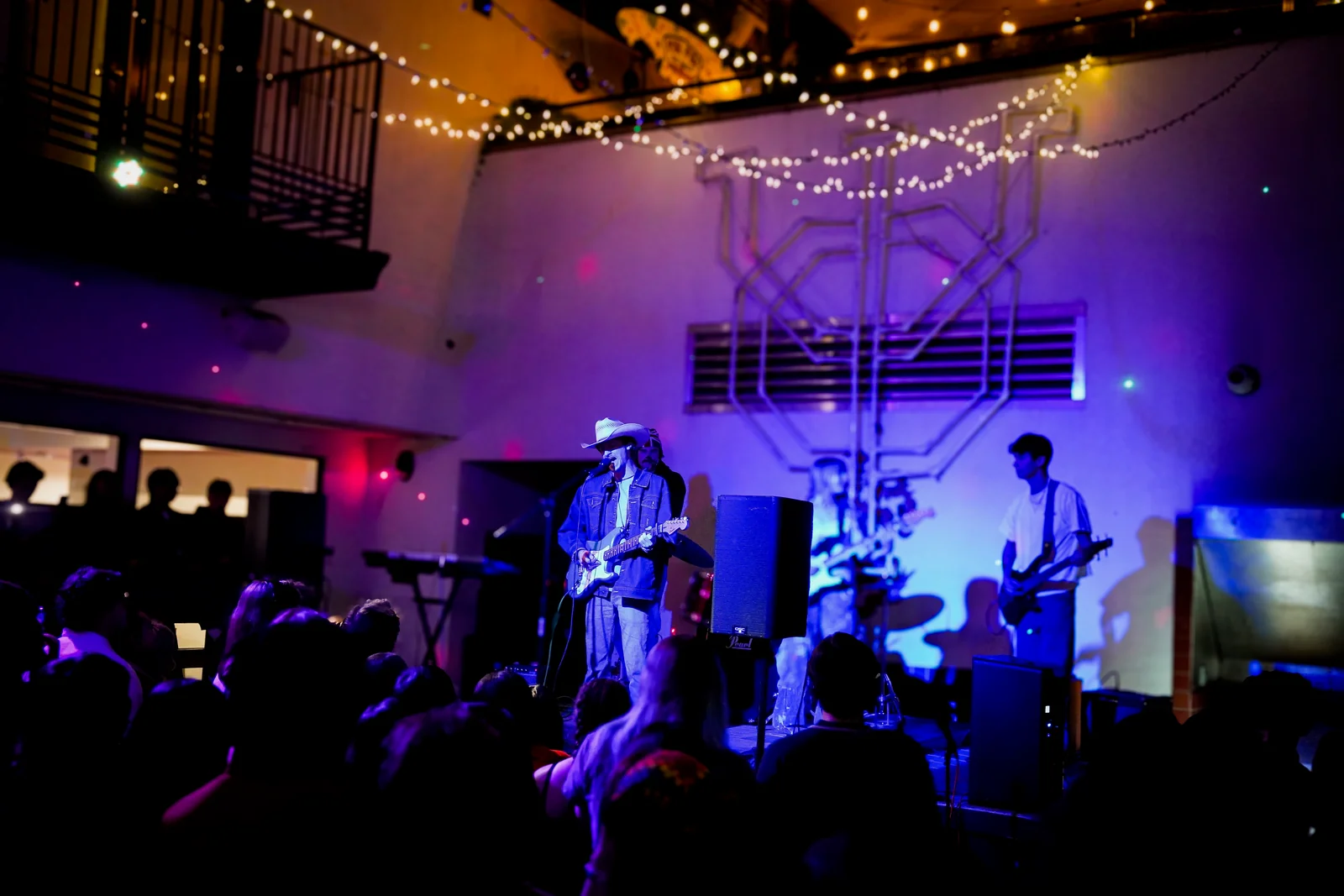 Miles and South of Sober performing beneath warm string lights, with the crowd at the front of the stage